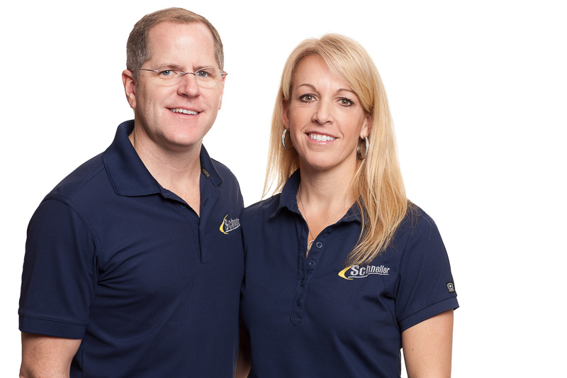 Schneller Knochelmann owners Kris and Lisa Knochelmann, standing together wearing navy blue polos. White background.