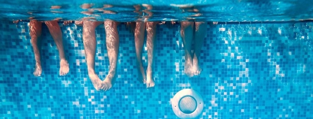 View of four people with their legs dangling over the edge of a swimming pool