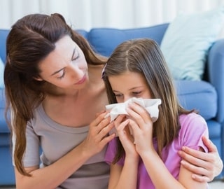 Mother comforting young girl who is sneezing into a tissue