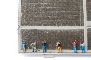 Tiny figurines of workers placed on an air filter, appearing to clean the filter