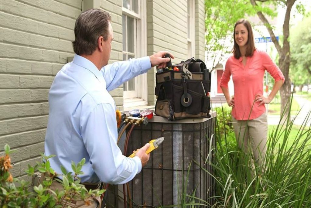 Technician speaking with woman while servicing air conditioning unit