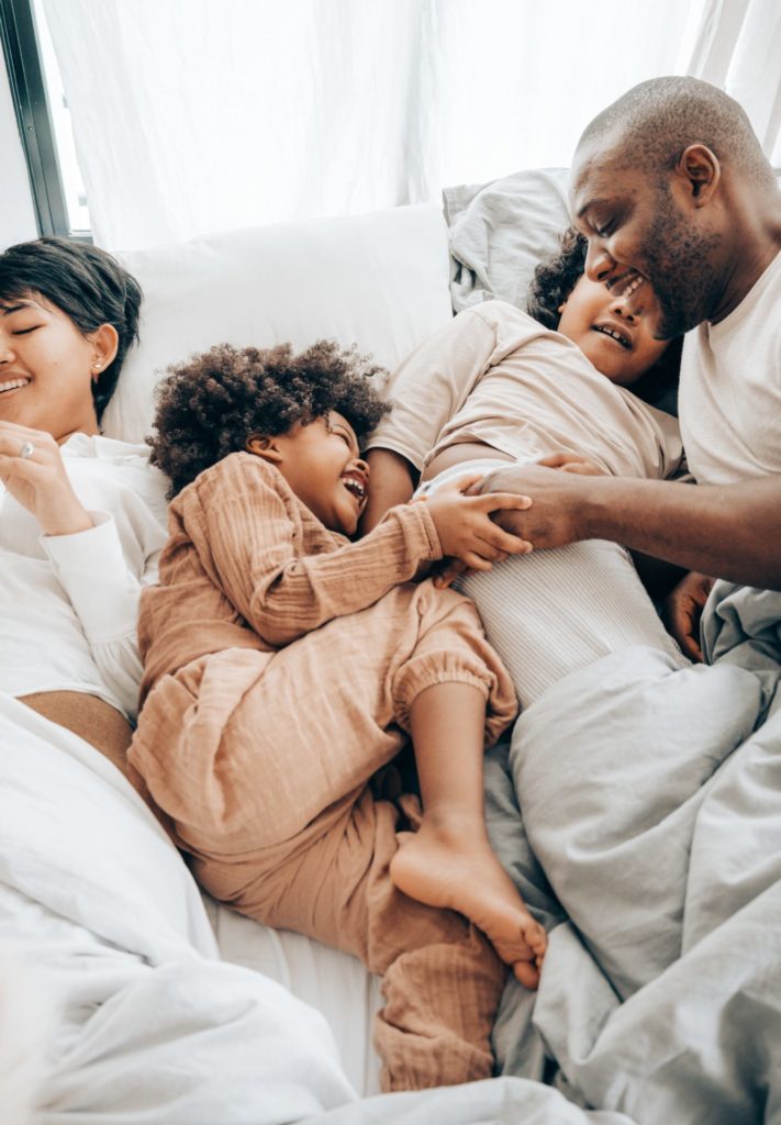 African American family of four snuggling and playing in bed.